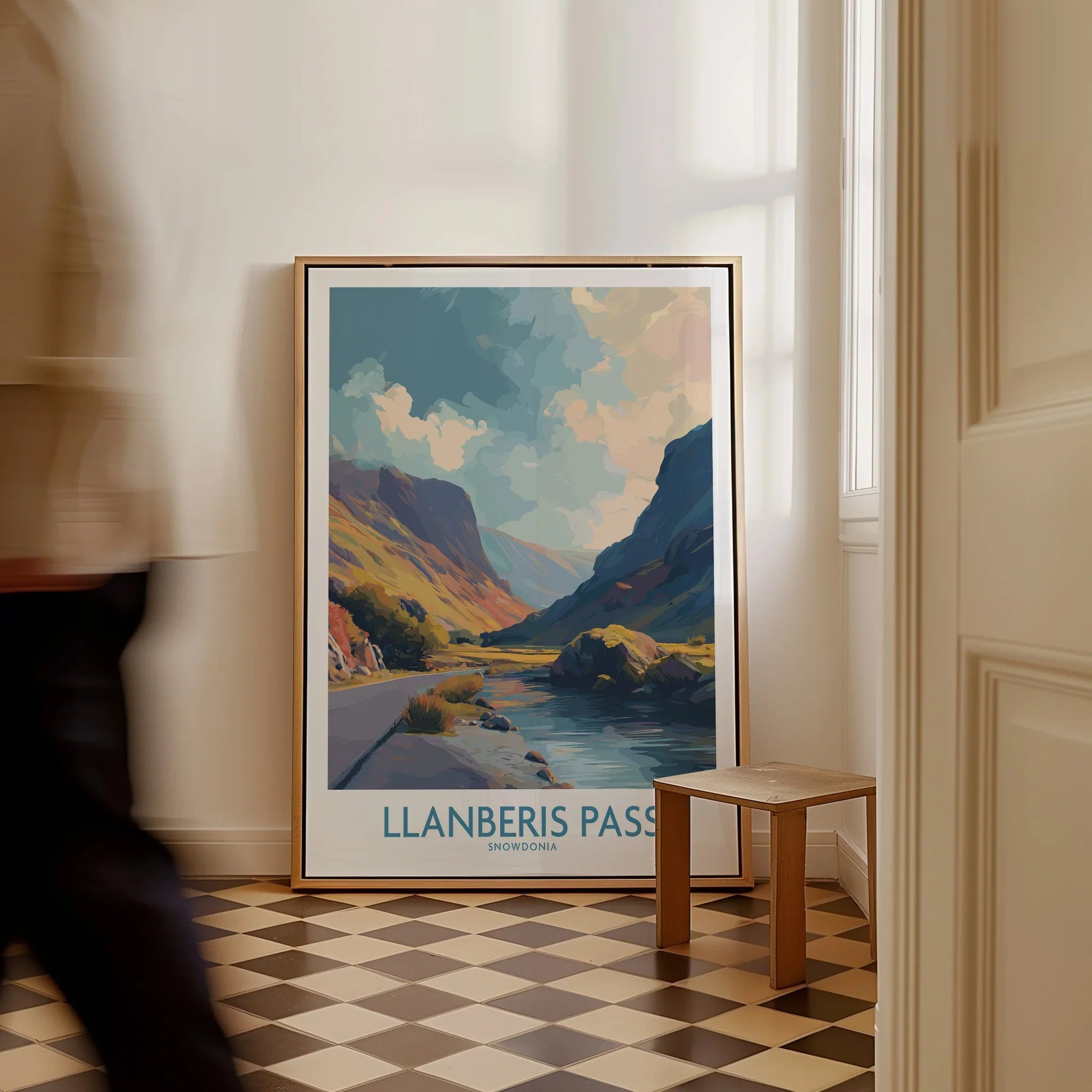 Framed Llanberis Pass travel poster on checkered floor in bright hallway, man walking by