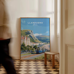 Framed Llandudno Wales travel poster on floor in hallway, man walking past