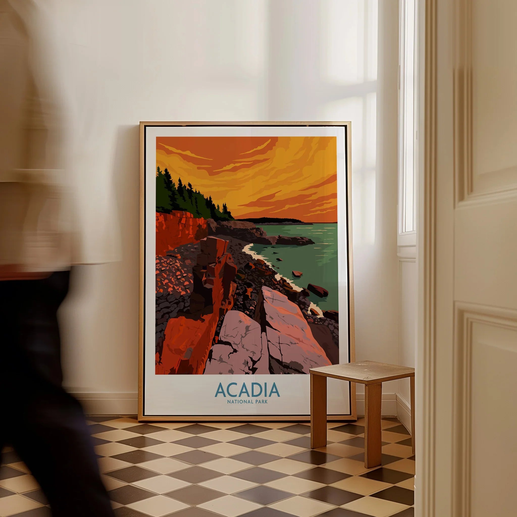 Framed Acadia National Park print with rocky coast and vibrant sunset beside a small bench indoors.