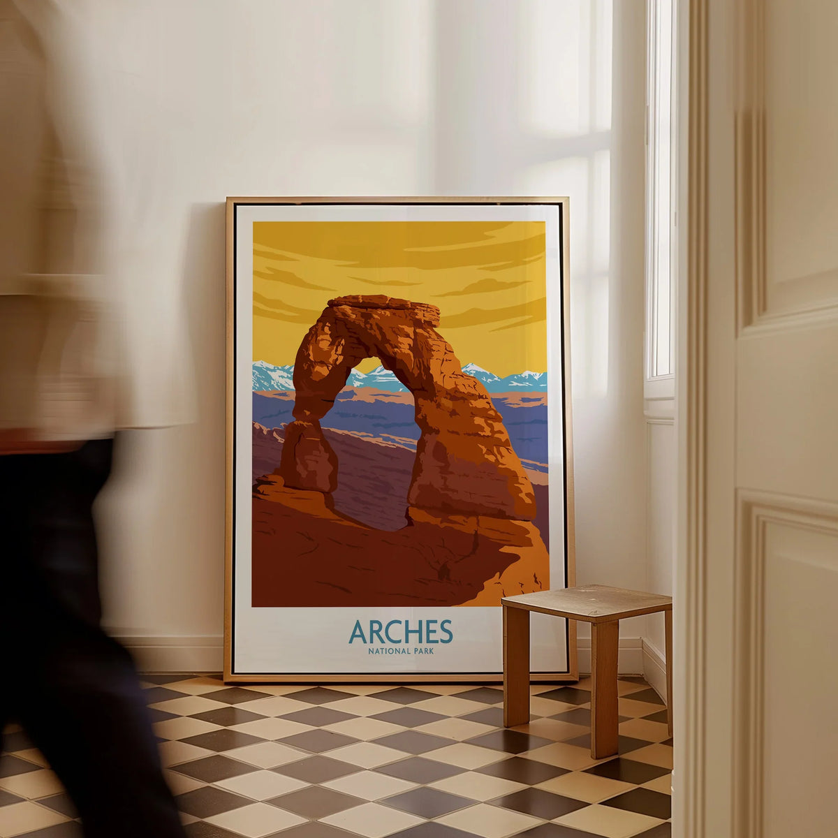 Framed Arches National Park travel poster on floor, man walking past in modern home