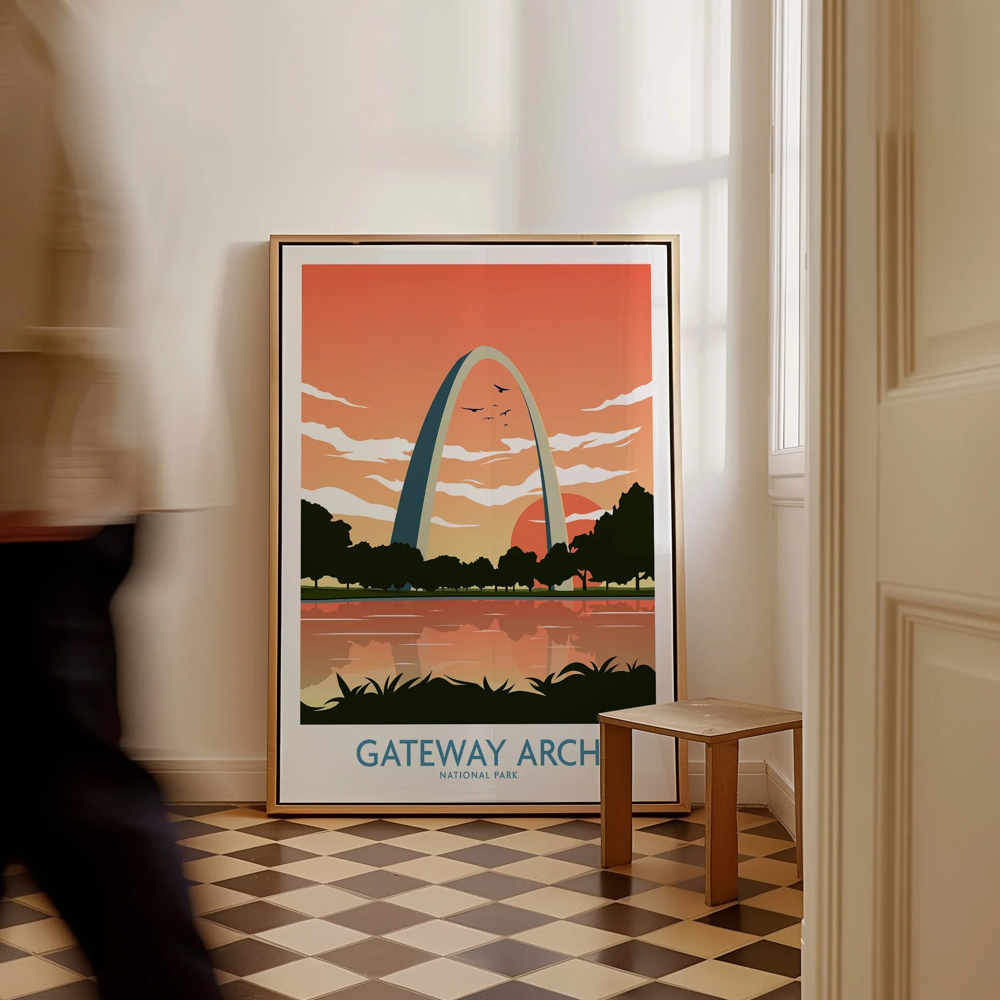 Framed Gateway Arch National Park travel poster on checkered floor, man walking past.