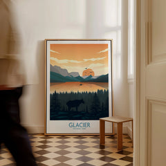 Framed Glacier National Park travel poster with mountain sunset, trees, and silhouette moose, on floor in hallway.