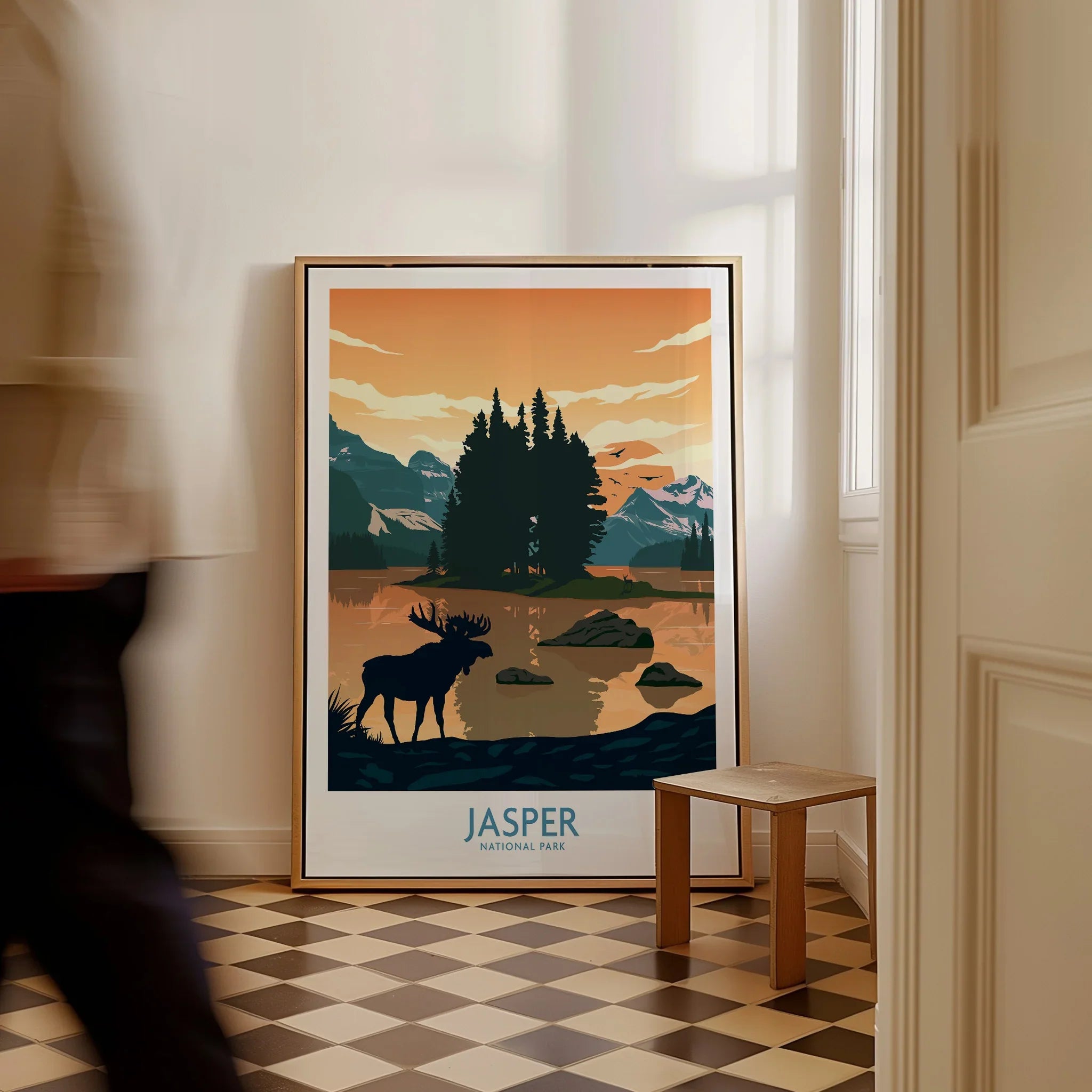 Framed Jasper National Park travel poster with moose and mountain landscape on floor indoors.