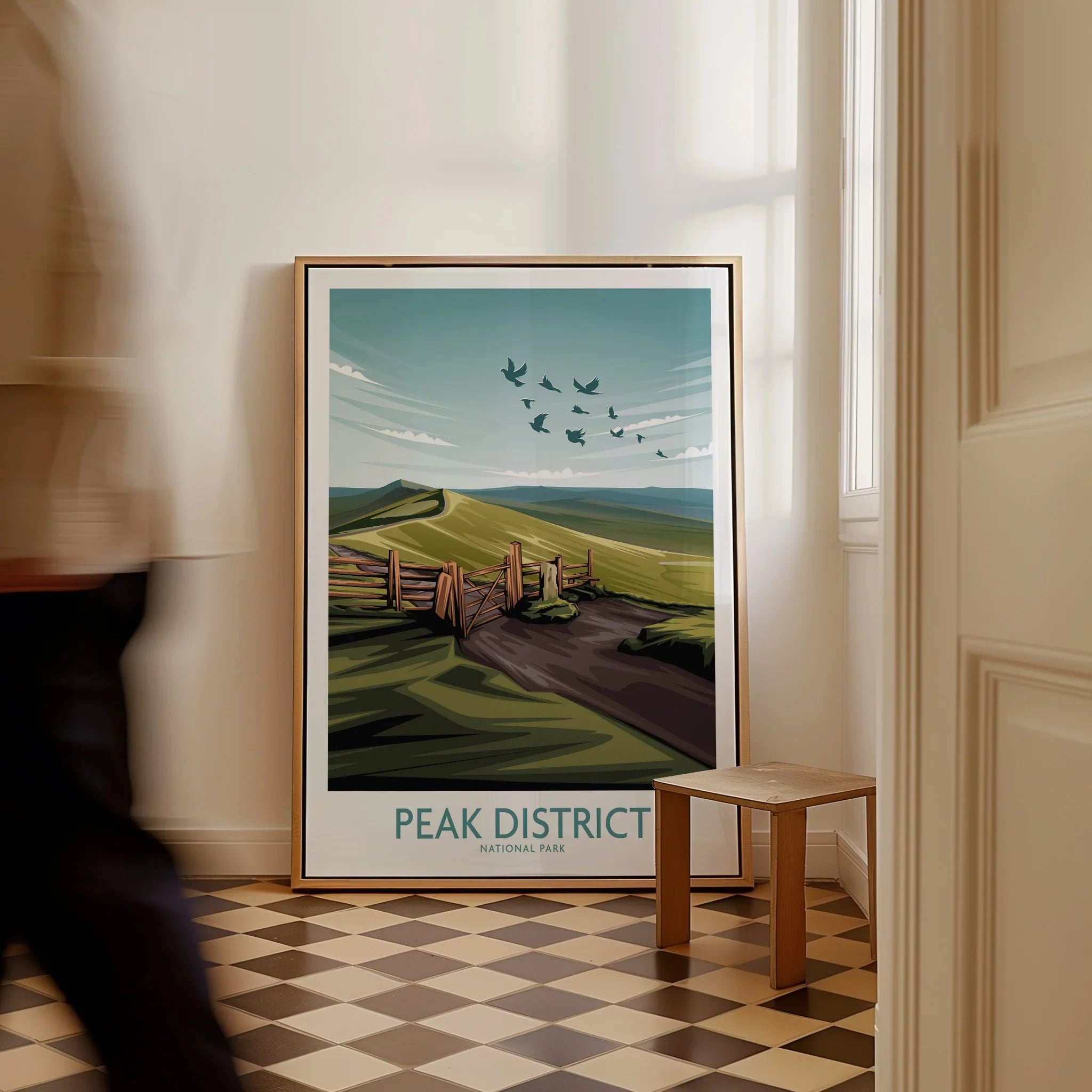 Framed Peak District National Park travel poster on floor in bright hallway, person walking past