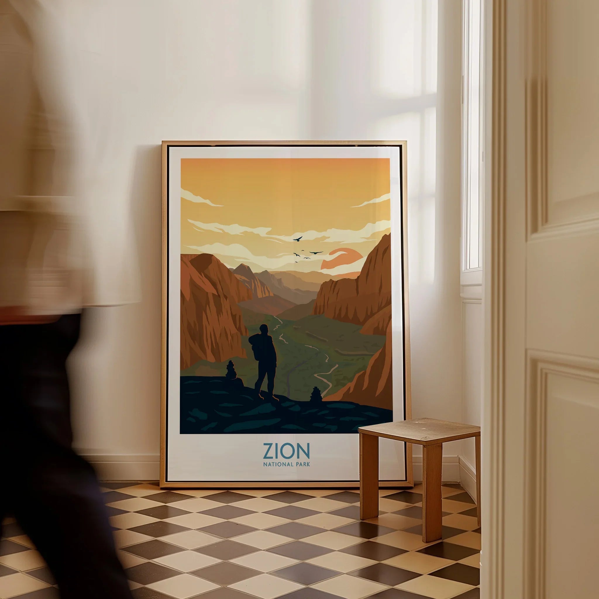 Framed Zion National Park art print with hiker, leaning on floor by a window.