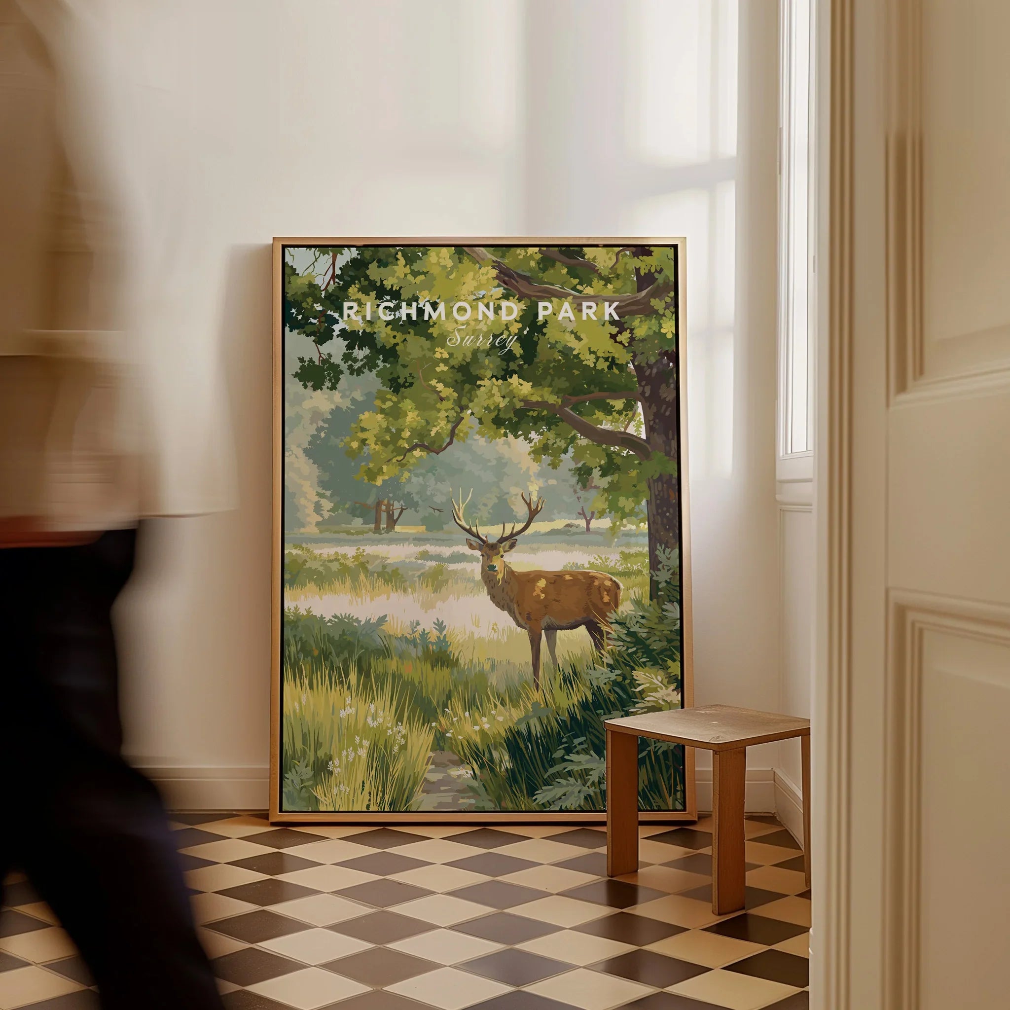 Framed Richmond Park travel poster with deer resting on floor in sunlit hallway