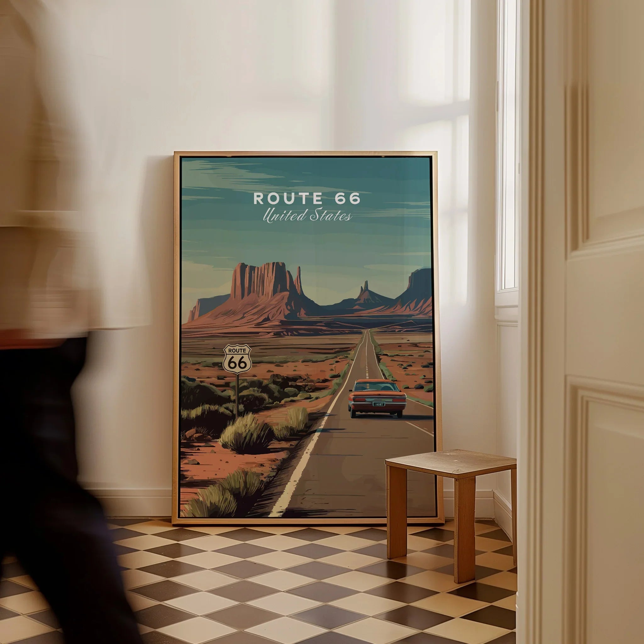 Framed Route 66 travel poster with vintage car and desert landscape on floor in bright room.