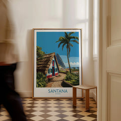 Framed Santana Madeira travel poster with A-frame house and palm tree, leaning on floor in bright hallway.