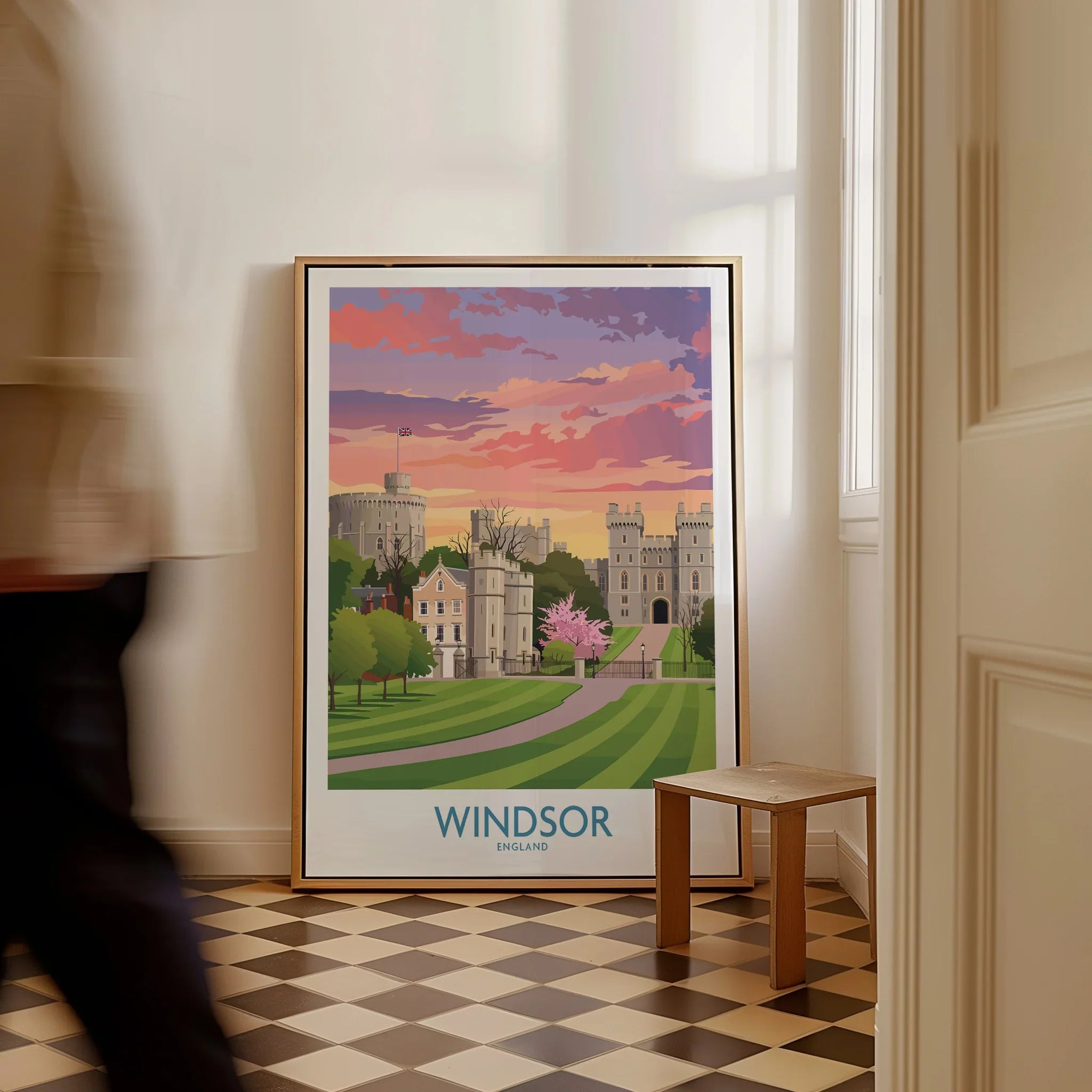 Framed Windsor England travel poster with scenic castle art, leaning on floor in bright hallway.