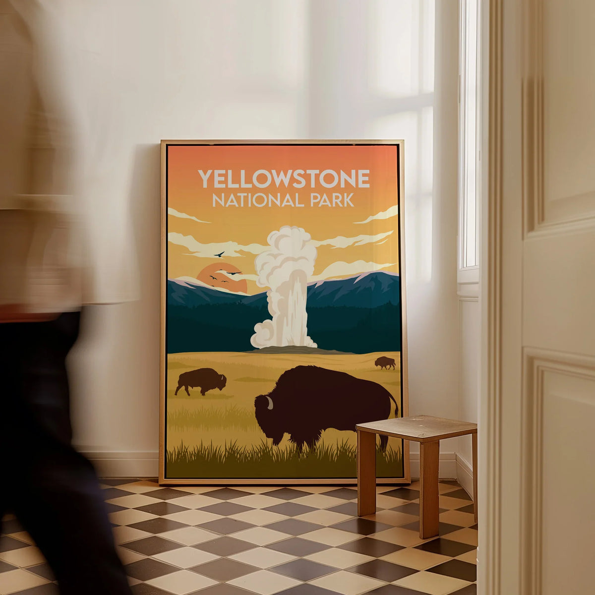 Yellowstone National Park framed poster with bison and geyser leaning on floor, man walking past.