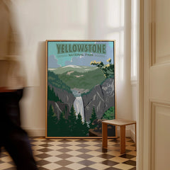 Framed Yellowstone National Park print with waterfall and mountains, on floor by a wall.