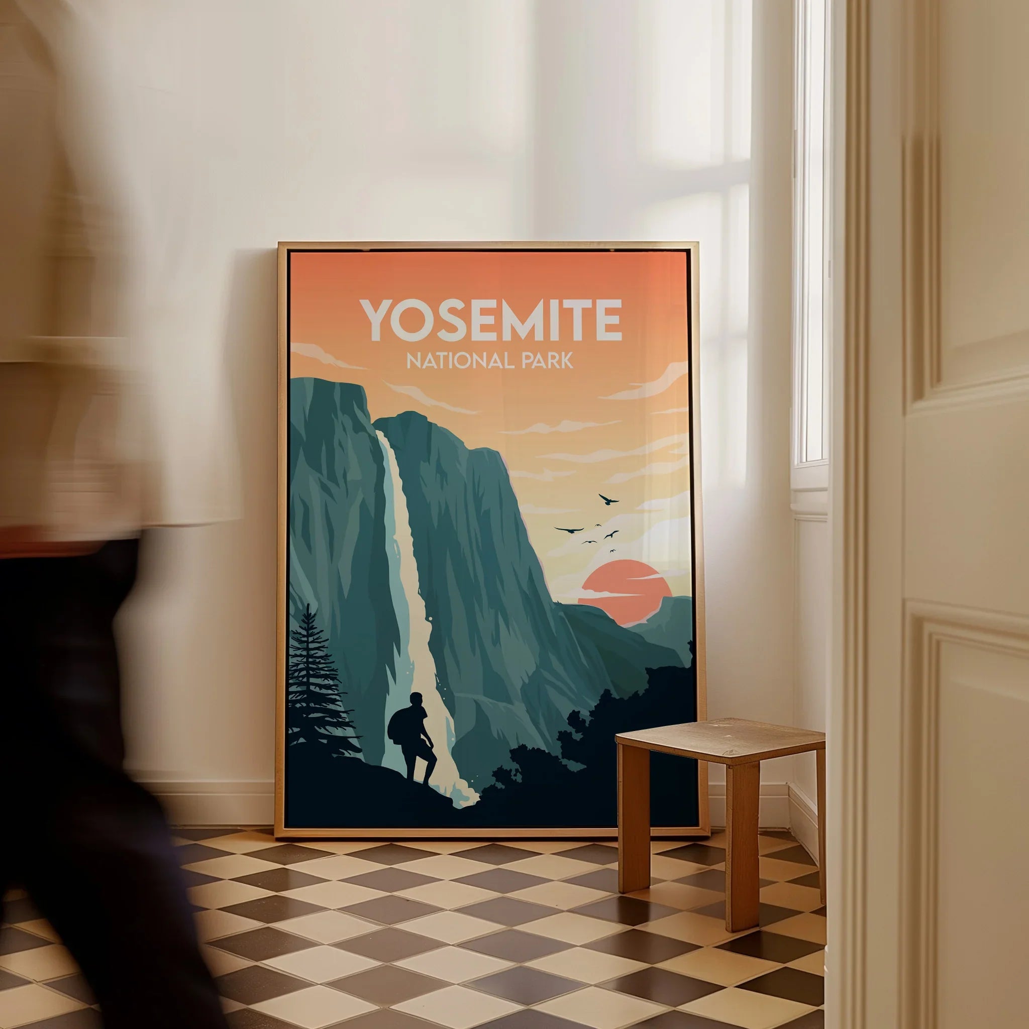Framed Yosemite National Park travel poster on floor in sunlit room, man walking past