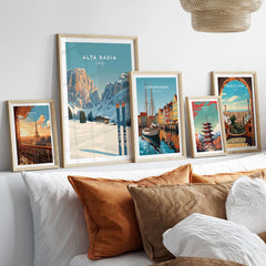 Framed Alta Badia Italy Ski Resort print among other travel posters on a sofa, showcasing alpine beauty and adventure.