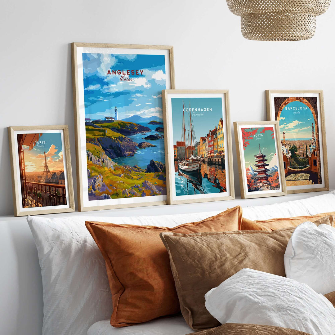 Framed Anglesey Wales poster with rocky coast lighthouse among other city posters on a cozy sofa.