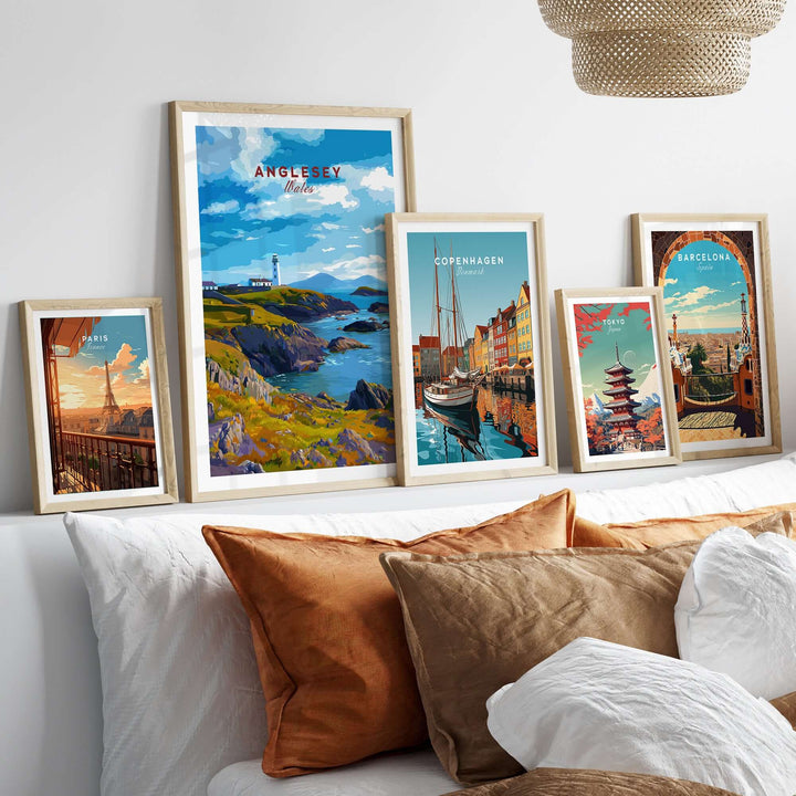 Framed Anglesey Wales poster with rocky coast lighthouse among other city posters on a cozy sofa.