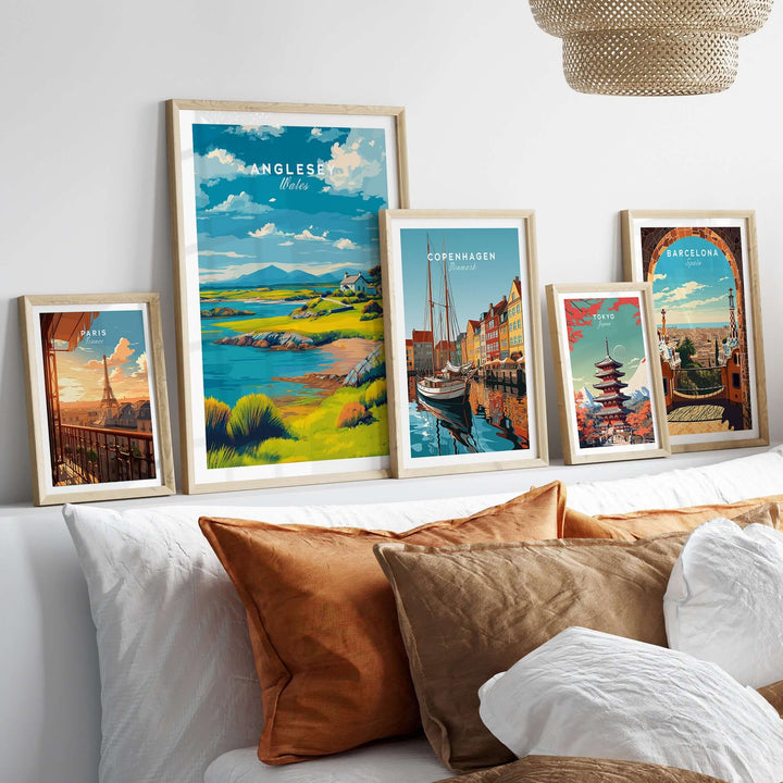 Framed prints of Anglesey, Copenhagen, Barcelona, and other landscapes on a cozy bed with decorative cushions.