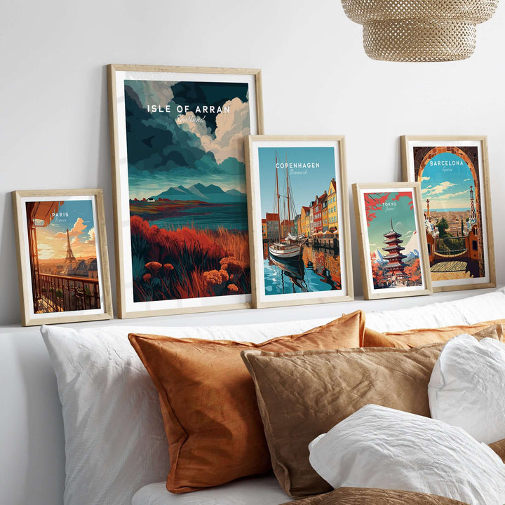Framed Isle of Arran wall art with other travel prints displayed above a cozy bed with decorative pillows.
