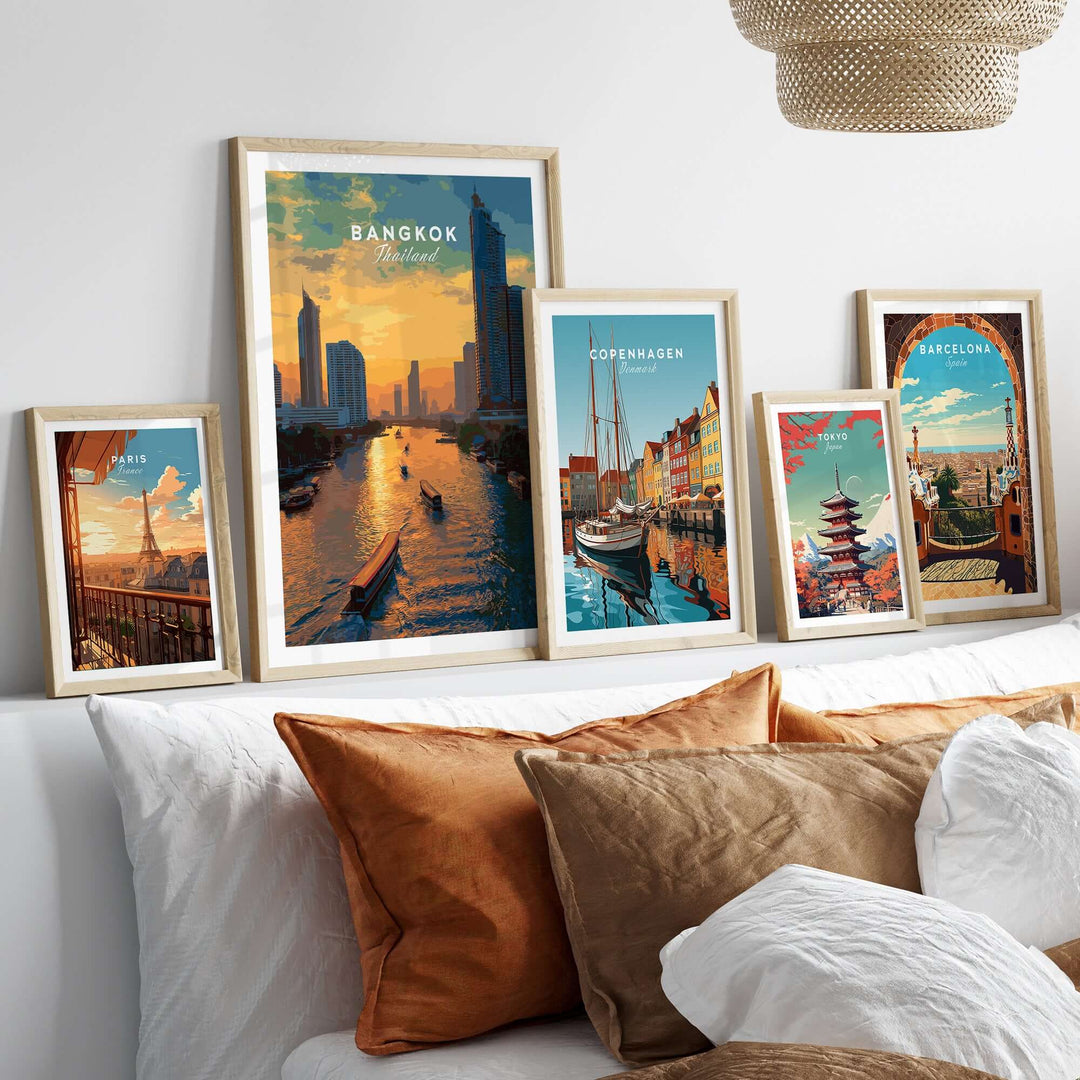 Framed prints of Bangkok, Copenhagen, and Barcelona cityscapes displayed on a cozy bed.