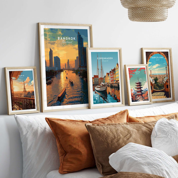Framed prints of Bangkok, Copenhagen, and Barcelona cityscapes displayed on a cozy bed.