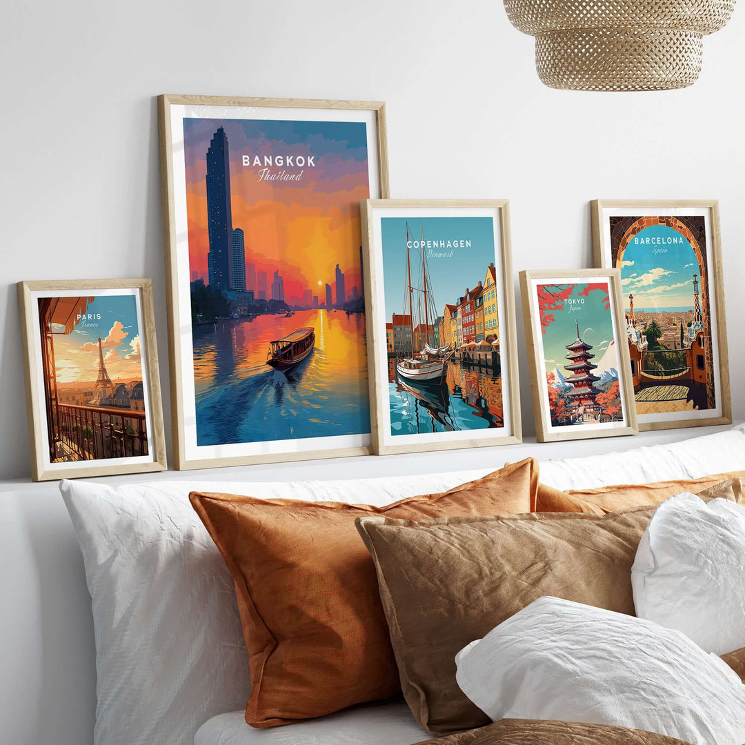 Framed posters of Bangkok, Copenhagen, and Barcelona above a bed with decorative pillows, showcasing vibrant cityscapes.
