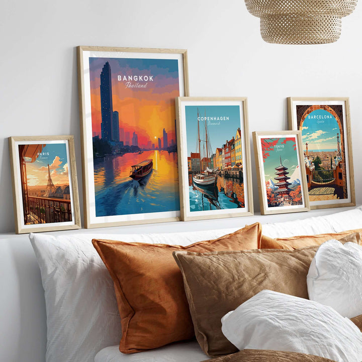 Framed posters of Bangkok, Copenhagen, and Barcelona above a bed with decorative pillows, showcasing vibrant cityscapes.