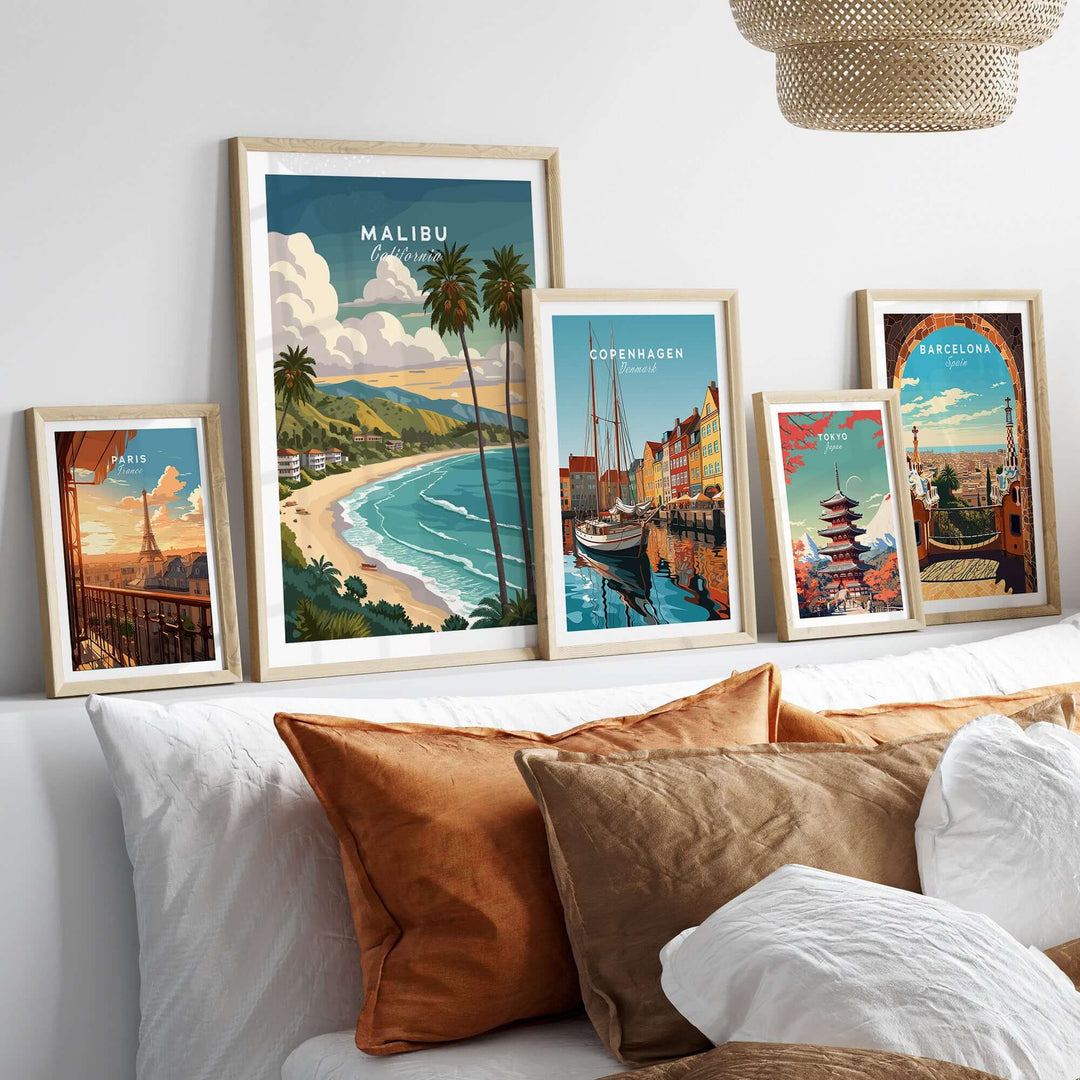 Framed Malibu California beach print alongside other city artwork on a cozy sofa.