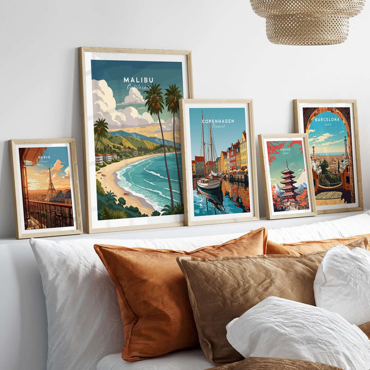 Framed Malibu California beach print alongside other city artwork on a cozy sofa.