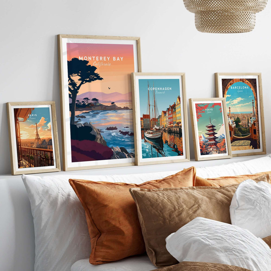 Framed posters of coastal landscapes including Monterey Bay, Copenhagen, and Barcelona on a cozy bed with decorative pillows.