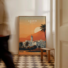 Agadir Travel Poster – Moroccan Mosque and Desert Sunset Art as a framed canvas leaning in a hallway with a chequered tiled floor