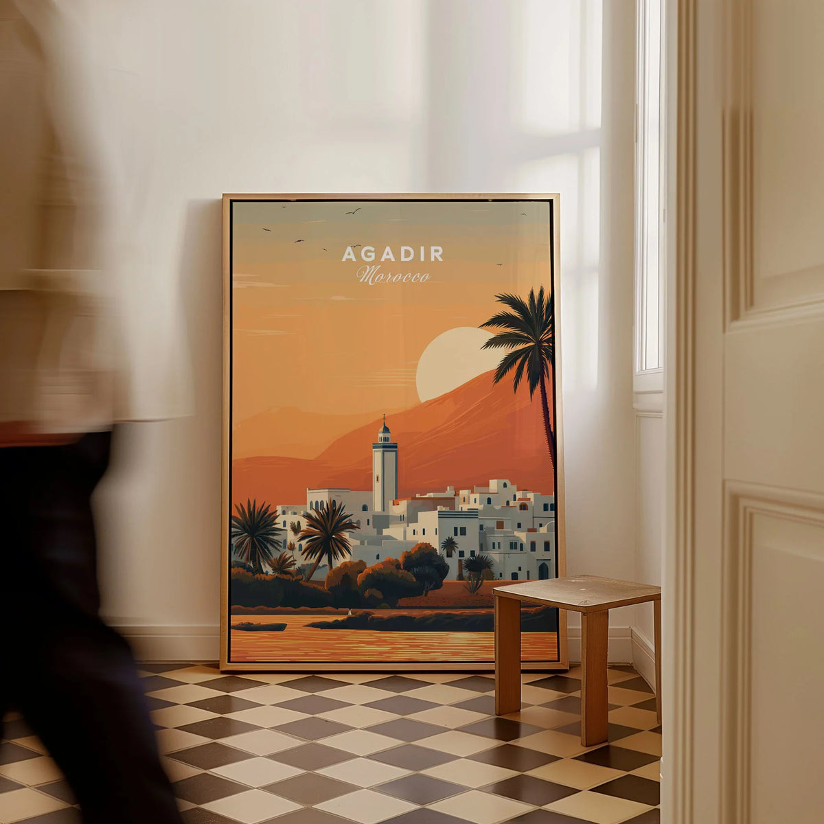 Agadir Travel Poster – Moroccan Mosque and Desert Sunset Art as a framed canvas leaning in a hallway with a chequered tiled floor