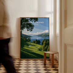Loch Lomond Scotland Summer Shore Travel Poster — a sunlit grassy shoreline running down to Loch Lomond under old oaks, shown as framed canvas on floor man walking past