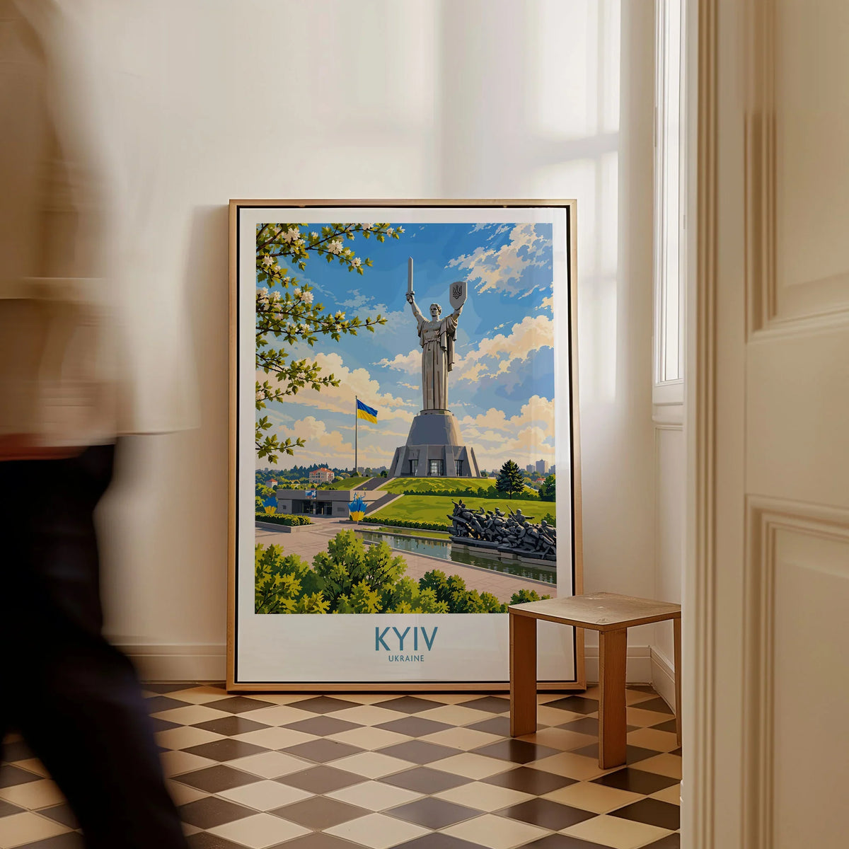 Kyiv Ukraine Spring Blossom Wall Art — the Motherland Monument under spring blossom with the Ukrainian flag flying, shown as framed canvas on floor man walking past