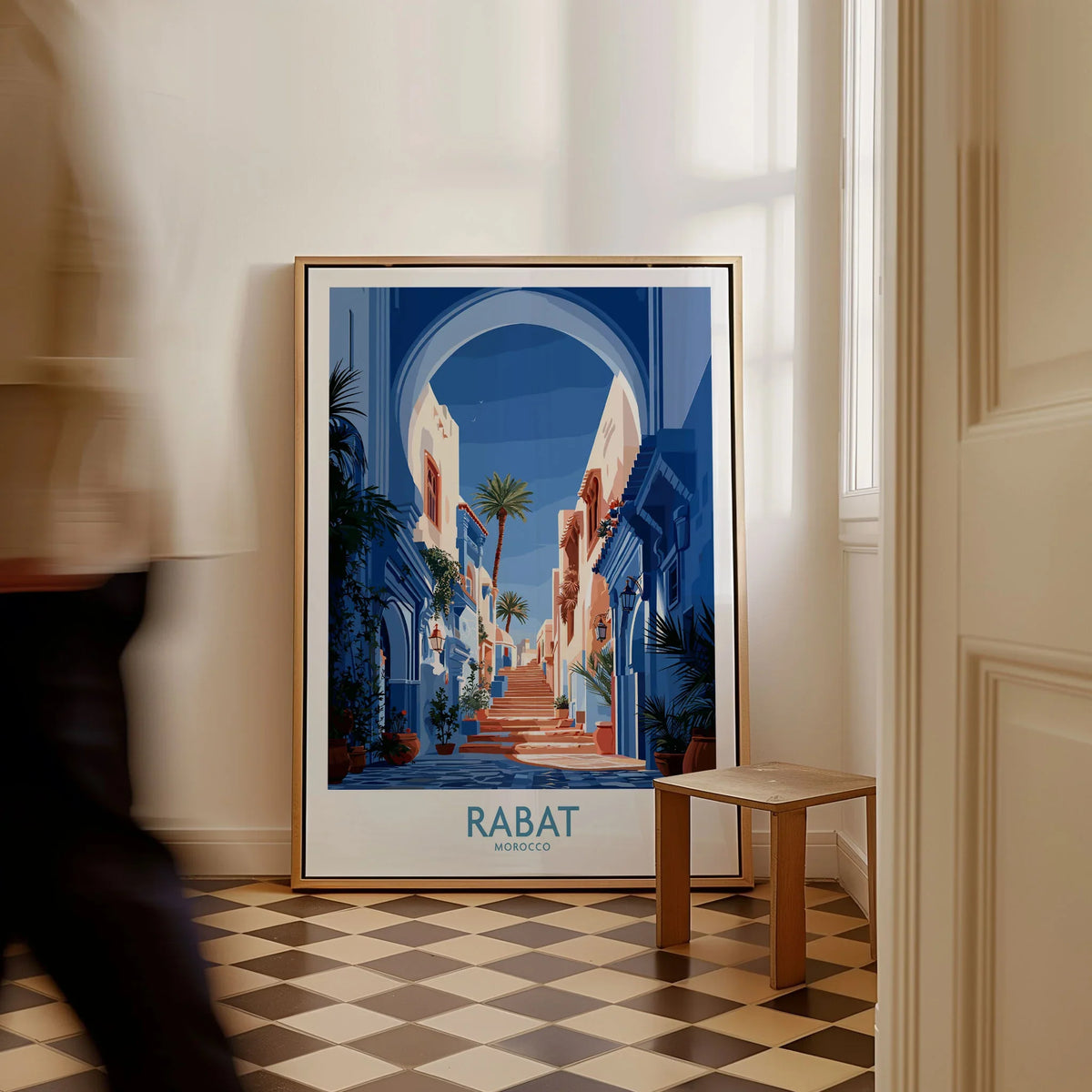 Rabat Morocco Blue Alleyway Wall Art — a blue-washed medina lane and stone steps seen through a horseshoe arch, shown as framed canvas on floor man walking past