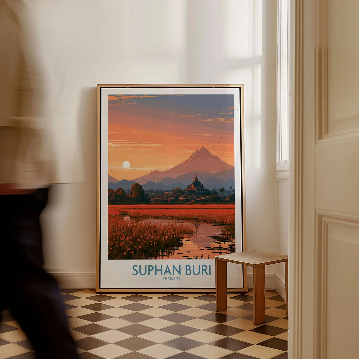 Suphan Buri Thailand Temple Sunset Wall Art — a lotus-covered lake and temple spire at sunset beneath a mountain peak, shown as framed canvas on floor man walking past
