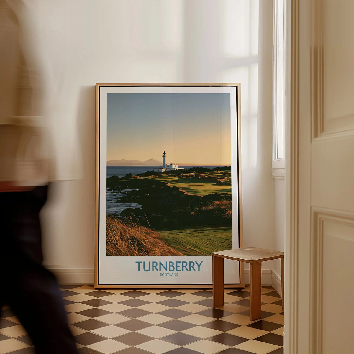 Turnberry Scotland Rocky Shore Wall Art — the Turnberry lighthouse above a rocky shore with the Arran hills beyond, shown as framed canvas on floor man walking past