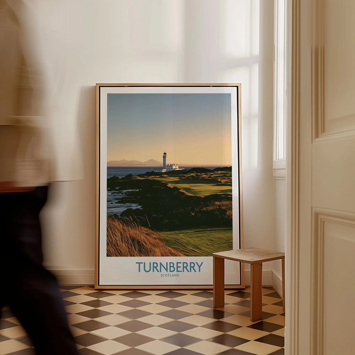 Turnberry Scotland Rocky Shore Wall Art — the Turnberry lighthouse above a rocky shore with the Arran hills beyond, shown as framed canvas on floor man walking past