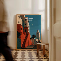 Tangier Morocco Kasbah Steps Travel Poster — coral kasbah steps climbing towards a minaret under a crescent moon, shown as framed canvas on floor man walking past