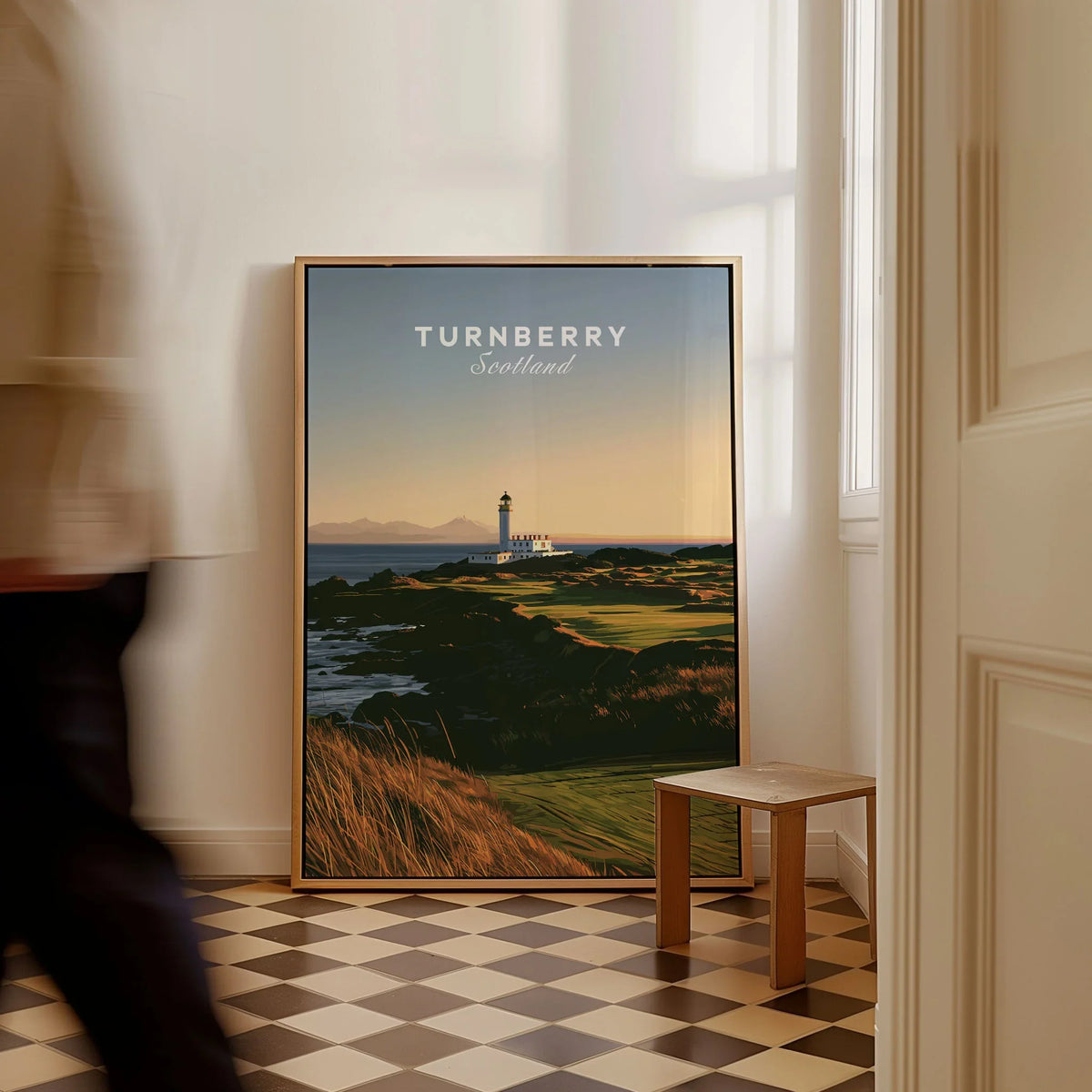 Turnberry Scotland Lighthouse Travel Poster — the Turnberry lighthouse above a rocky shore with the Arran hills beyond, shown as framed canvas on floor man walking past