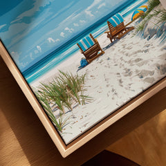 Framed canvas wall art of a beach scene with chairs, sand, and blue ocean.
