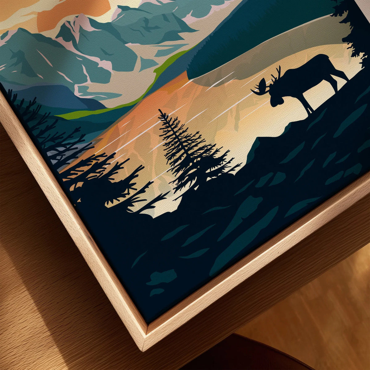 Close-up of framed canvas wall art with silhouette of moose, pine trees, mountains, and sunset.