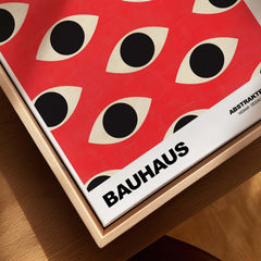 Bauhaus Exhibition Prints - Repeating Eyes Pattern Poster Red Black Cream Art displayed in a wooden frame with abstract eye design.