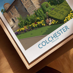 Close-up of Colchester England travel poster in natural wood floating frame with castle and gardens.