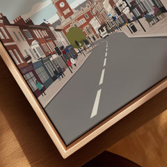Close-up of city street art print with natural wood floating frame on table