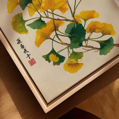 Close-up of framed canvas wall art with ginkgo leaves and Asian calligraphy in natural wood floating frame