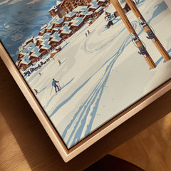 Close-up of framed canvas wall art showing a snowy ski village and skiers in winter landscape.