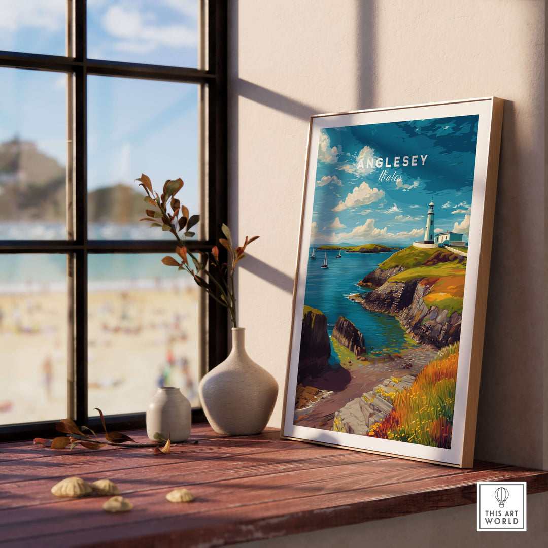 Anglesey Wales sailboats and lighthouse coastal wall art print displayed by a window with a beach view.