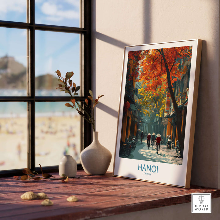 Framed Hanoi wall art depicting traditional Vietnamese life in vibrant autumn colors by a sunny beach window.