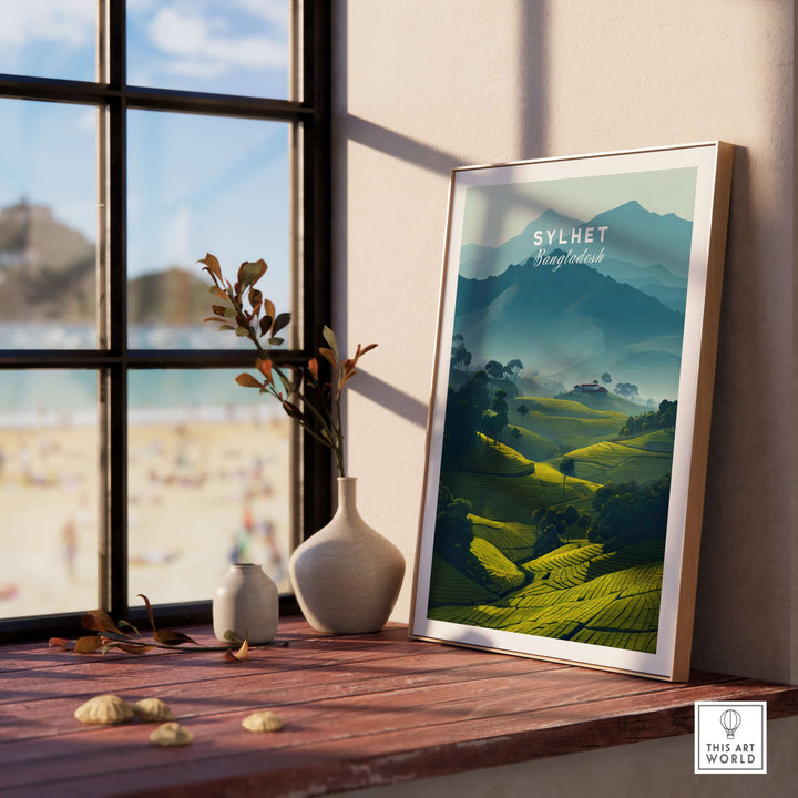 Sylhet Bangladesh poster featuring lush tea plantations and misty mountains, displayed on a windowsill with a beach view.