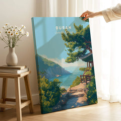 Hand holding Busan South Korea travel poster canvas with coastal landscape in modern room