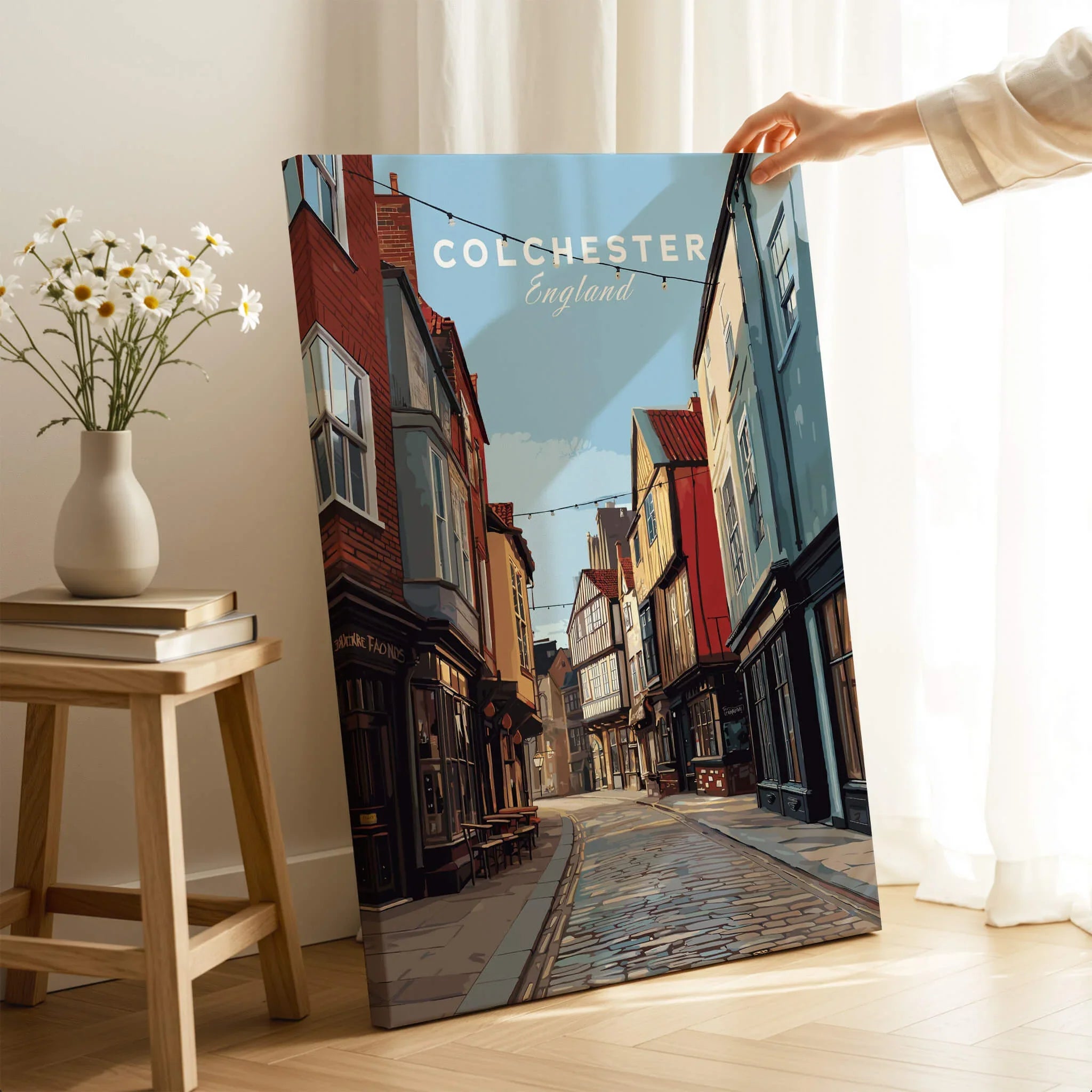 Hand holding Colchester England travel poster canvas print in cozy room with daisies